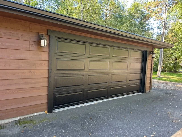 Bronze raised-panel garage door with windows installed on a stone-and-cedar Midwest home